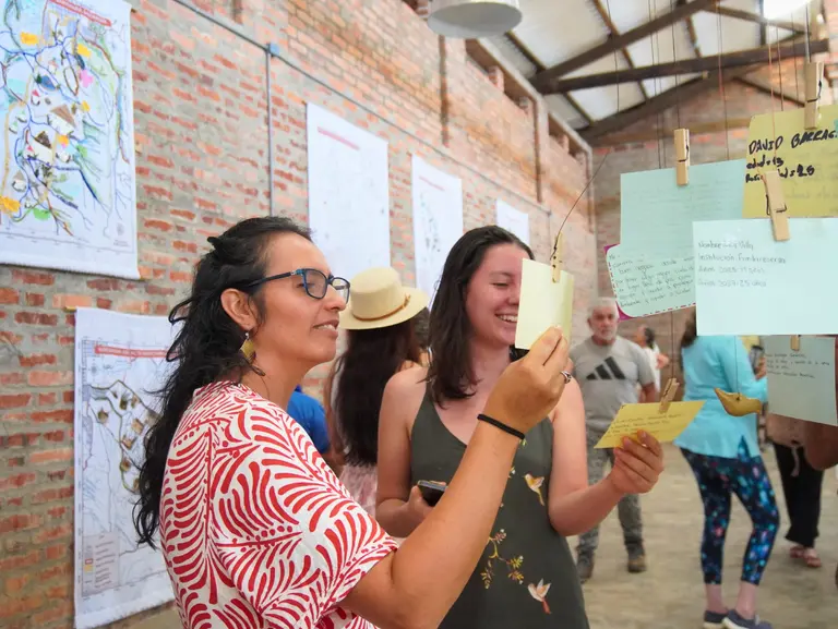 Mujeres revisando notas en una pared con mapas, parte del proyecto "De la palabra a la acción: el EOT".