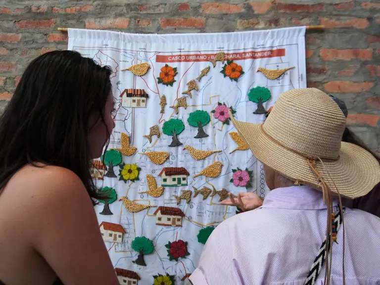 Mujeres viendo mapa artesanal de Barichara, Santander. "Casco Urbano - Barichara, Santander" es visible en el mapa.
