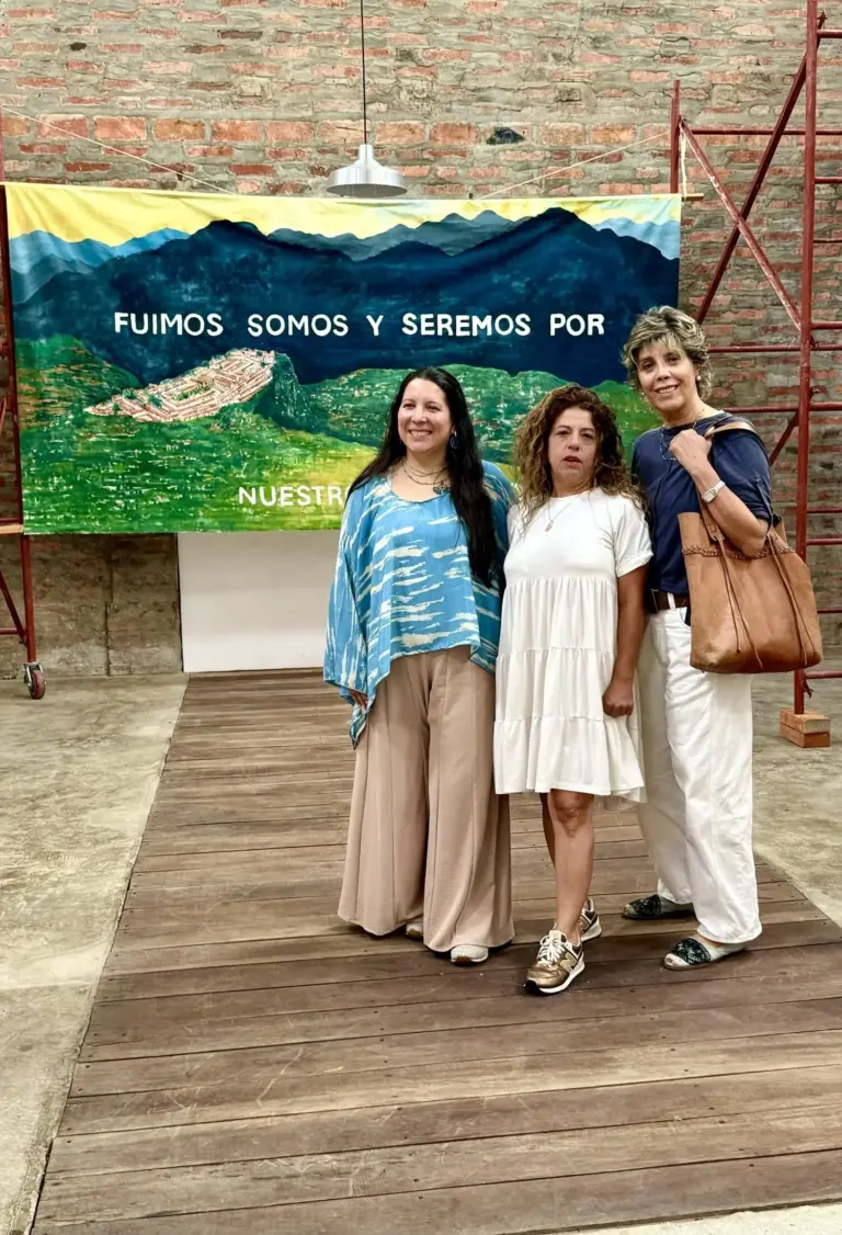 Tres mujeres frente a un cartel con el texto "Fuimos, somos y seremos por nuestra". Visita en Barichara.
