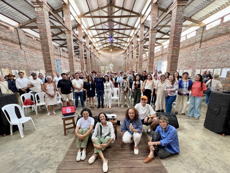 Grupo grande en el Foro Ciudadano EOT Barichara, con panelistas sentados al frente. Arquitectura de ladrillo vista.