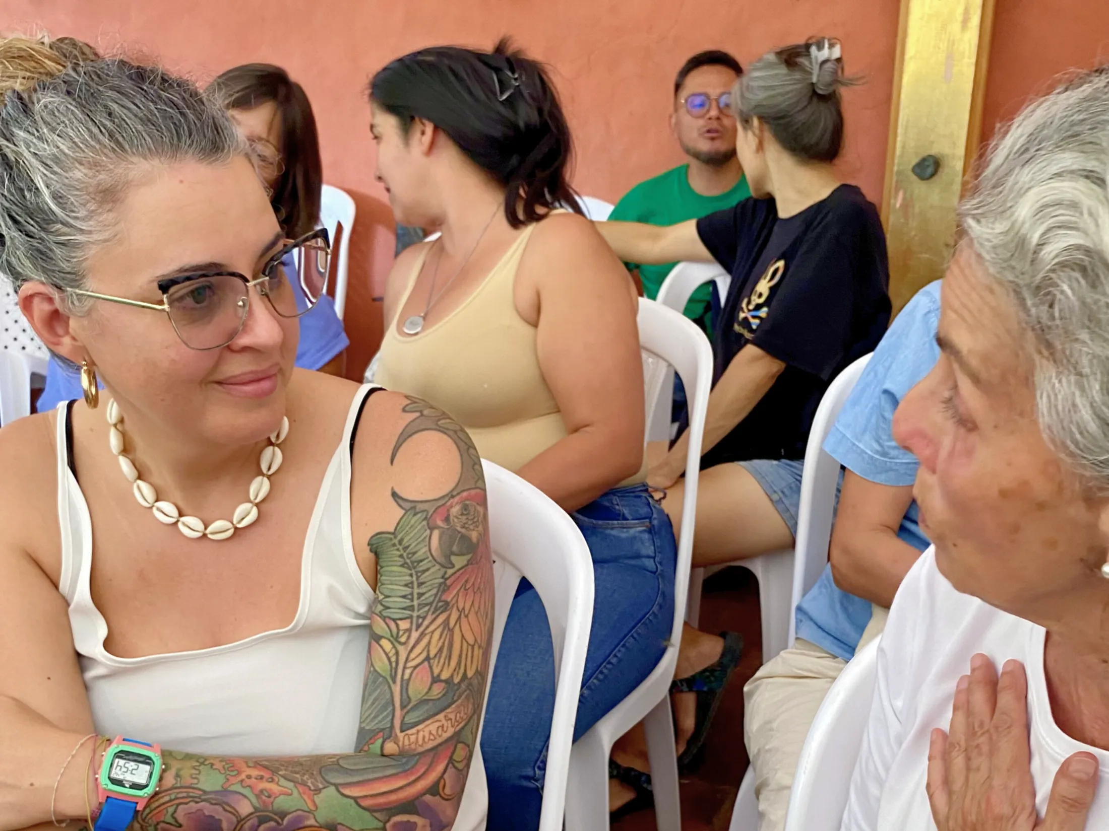 Mujeres conversando en intercambio cultural, con tatuajes y collares. Tejiendo puentes.