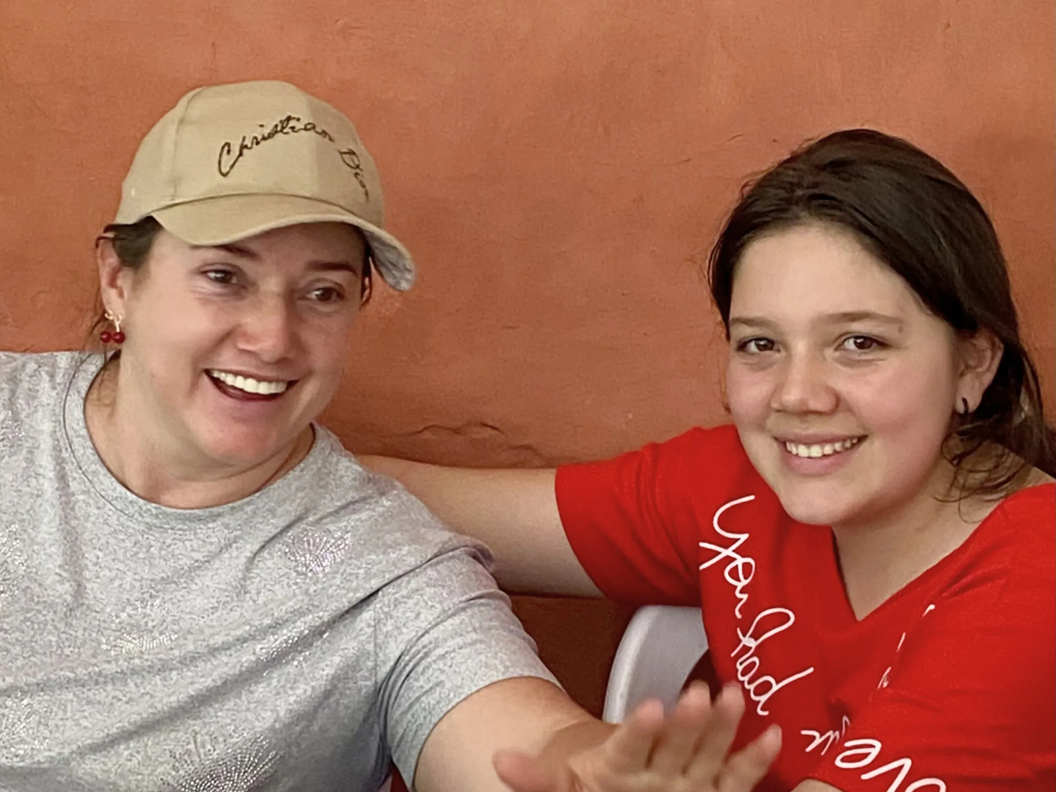 Dos mujeres sonriendo juntas. Una lleva gorra "Christian Dior". Intercambio cultural Kairigua y Rizoma.