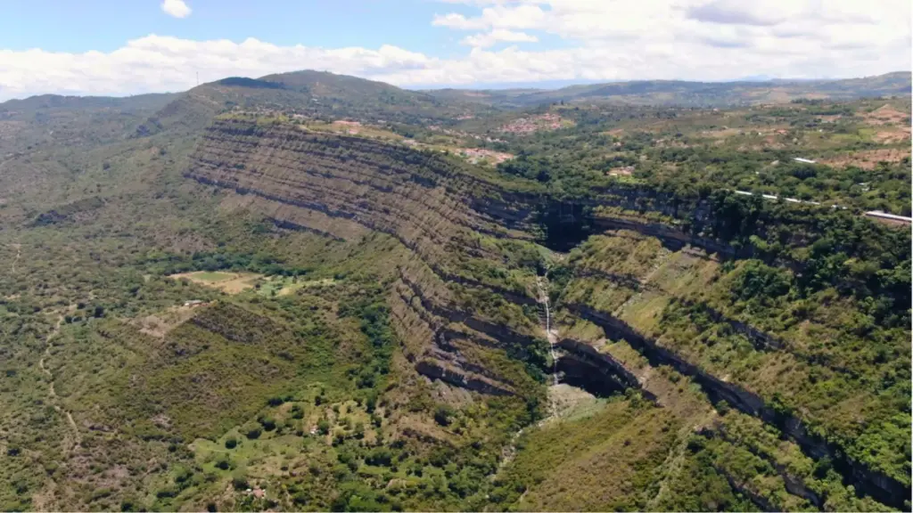 Paisaje montañoso con cascada en Raizagua, microcuenca de La Paramera. Vegetación exuberante y cielo azul.