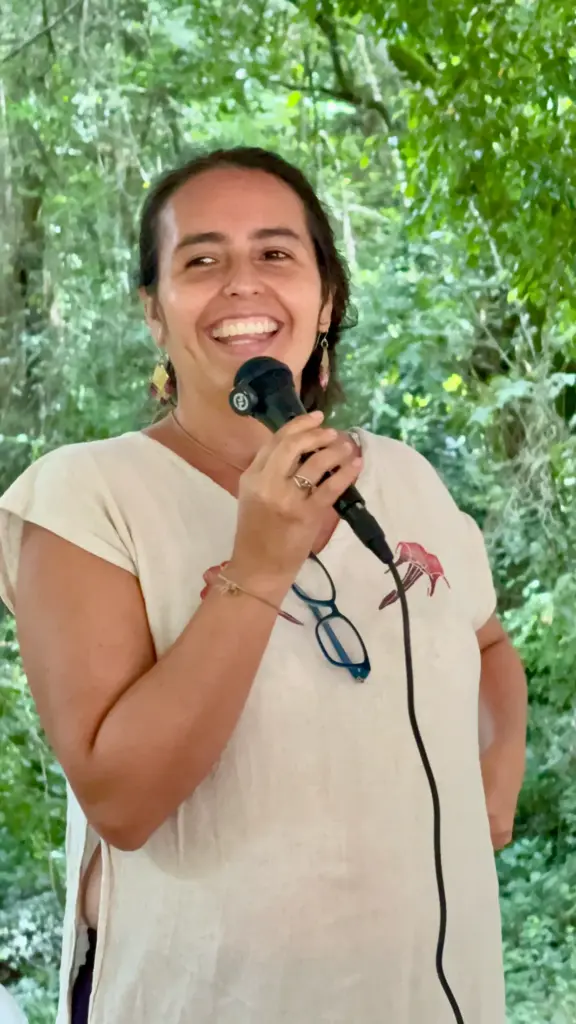 Mujer sonríe hablando en un micrófono en un evento al aire libre
