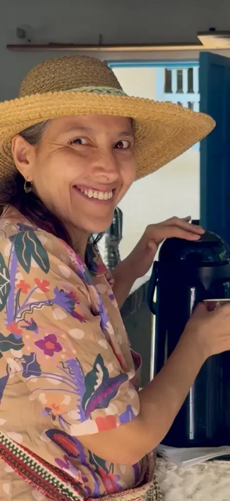 Mujer sonriente con sombrero de paja y blusa floral sirviendo de un termo